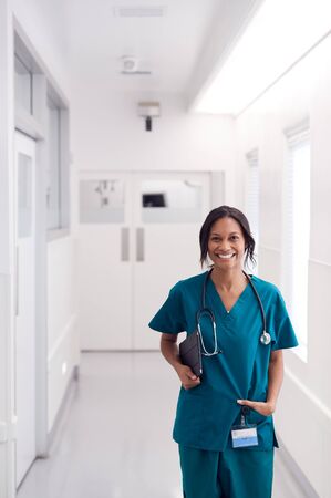 Portrait Of Smiling Female Doctor Wearing Scrubs In Hospital Corridor Holding Digital Tabletの写真素材