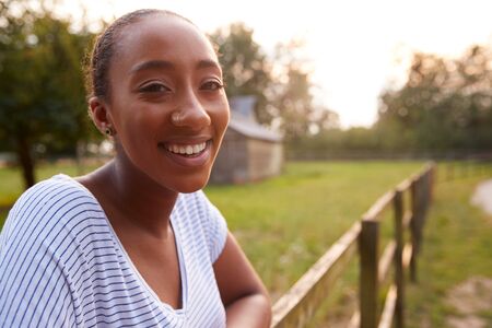 Portrait Of Smiling Young Woman Taking A Break And Resting On Fence During Walk In Countrysideの写真素材