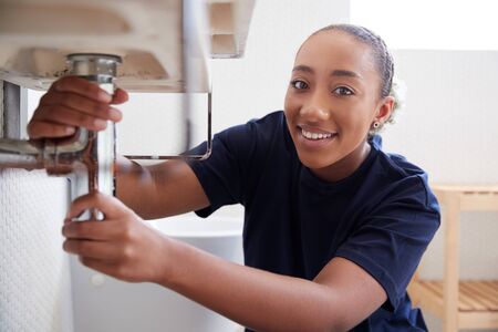 Portrait Of Female Plumber Working To Fix Leaking Sink In Home Bathroomの写真素材
