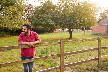 Smiling Man Taking A Break And Resting On Fence During Walk In Countrysideの写真素材