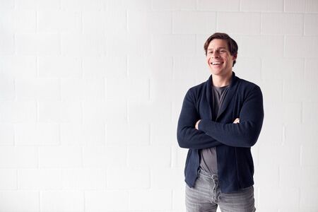 Portrait Of Casually Dressed Smiling Man Standing Against White Studio Wall