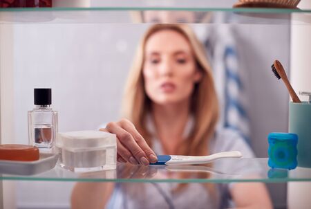 View Through Bathroom Cabinet Of Anxious Woman Waiting For Home Pregnancy Test Result