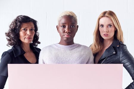 Three Women Holding Blank Pink Card With Copy Space Standing Against White Studio Wallの写真素材