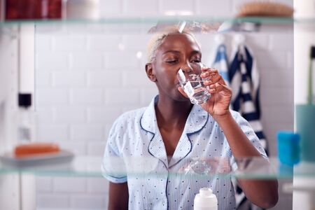View Through Bathroom Cabinet Of Woman Drinking Glass Of Waterの写真素材