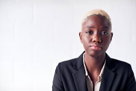 Portrait Of Determined Young Businesswoman Wearing Suit Standing Against White Studio Wallの写真素材