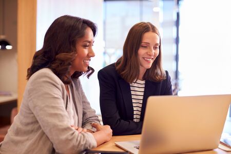 Two Businesswomen With Laptop Collaborating On Project In Office Together
