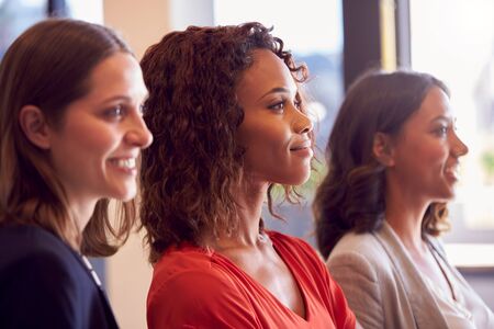 Three Businesswomen Standing In Modern Open Plan Office Together