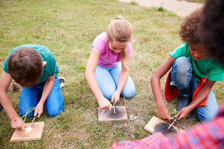 Team Leader Showing Group Of Children On Outdoor Camping Trip How To Make Fire