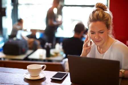 Woman In Coffee Shop Working On Laptop And Using Mobile Phoneの写真素材