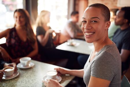 Portrait Of Smiling Woman Sitting At Table In Coffee Shopの写真素材