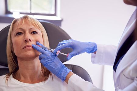 Mature Woman Sitting In Chair Being Give  Injection By Female Doctorの写真素材