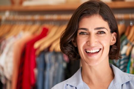 Portrait Of Smiling Female Owner Of Fashion Store Standing In Front Of Clothing On Rails
