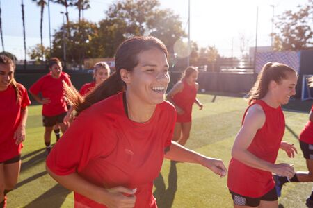 Womens Football Team Run Whilst Training For Soccer Match On Outdoor Astro Turf Pitchの写真素材