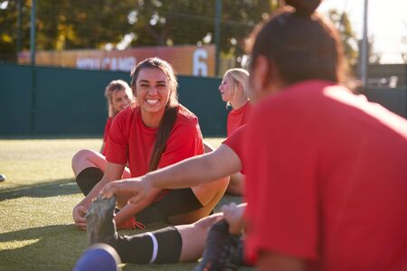 Womens Football Team Stretching Whilst Training For Soccer Match On Outdoor Astro Turf Pitch