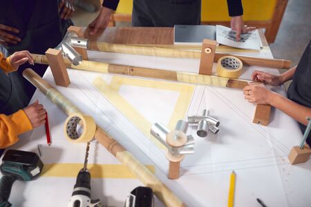 Close Up Of Multi-Cultural Team In Workshop Assembling Hand Built Bamboo Bicycle Frame