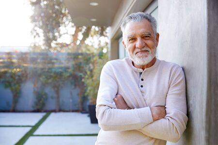 Portrait Of Smiling Retired Senior Hispanic Man In Garden At Home Against Flaring Sunの写真素材
