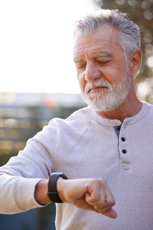Senior Hispanic Man Checking Health Monitor On Smart Watch In Garden At Homeの写真素材