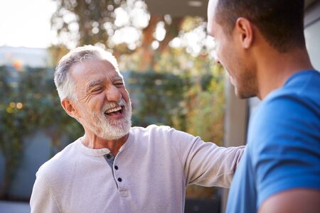 Senior Hispanic Man Talking And Laughing With Adult Son In Garden At Homeの写真素材