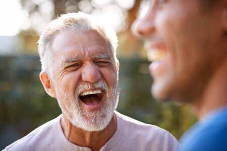 Senior Hispanic Man Talking And Laughing With Adult Son In Garden At Homeの写真素材