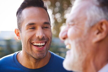 Senior Hispanic Man Talking And Laughing With Adult Son In Garden At Homeの写真素材