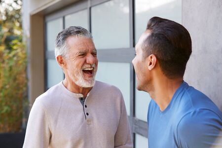 Senior Hispanic Man Talking And Laughing With Adult Son In Garden At Homeの写真素材