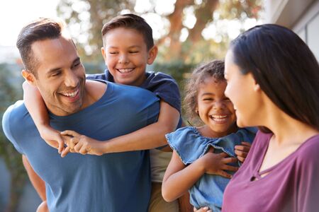 Smiling Hispanic Family With Parents Giving Children Piggyback Rides In Garden At Homeの写真素材
