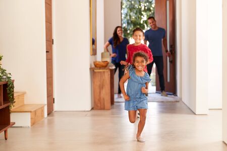 Excited Family Returning Home After Trip Out With Children Running Through Front Doorの写真素材