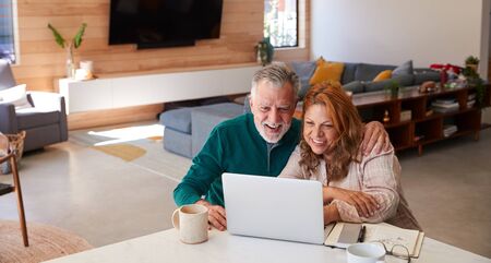 Senior Hispanic Couple At Home Sitting At Table Using Laptop Togetherの写真素材