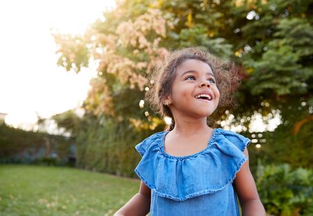 Young Hispanic Girl Having Fun Playing Outdoors In Gardenの写真素材