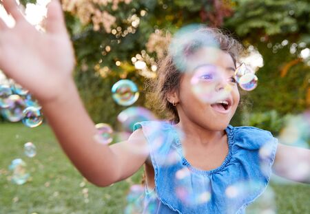 Young Hispanic Girl Chasing And Catching Bubbles In Gardenの写真素材