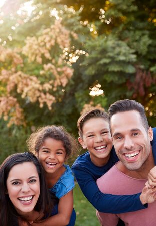 Portrait Of Smiling Hispanic Family With Parents Giving Children Piggyback Rides In Garden At Homeの写真素材