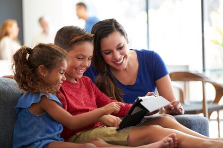 Mother Playing Video Games With Children On Digital Tablet During Family Gathering At Home