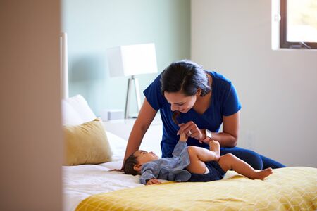 Mother Playing With Baby Daughter Lying On Bed At Homeの写真素材