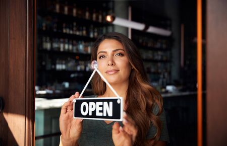 Female Owner Of Start Up Coffee Shop Or Restaurant Turning Round Open Sign On Doorの写真素材