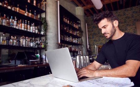 Male Owner Of Restaurant Bar Sitting At Counter Working On Laptopの写真素材