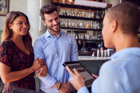 Couple Being Greeted By Maitre D Using Digital Tablet As They Arrive At Restaurantの写真素材