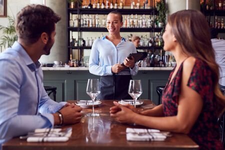 Female Waitress With Digital Tablet Taking Order From Romantic Couple Sitting At Restaurant Tableの写真素材