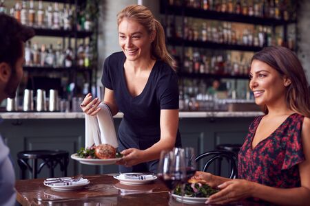 Female Waitress  Serving Food To Romantic Couple Sitting At Restaurant Tableの写真素材
