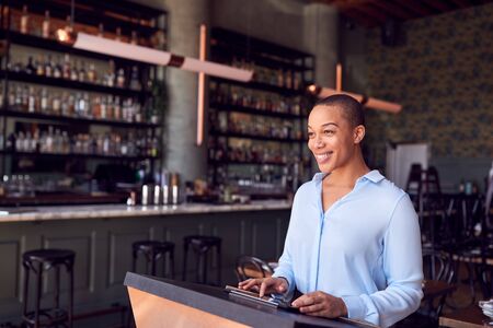 Female Owner Of Restaurant Bar Standing At Counter Using Digital Tabletの写真素材