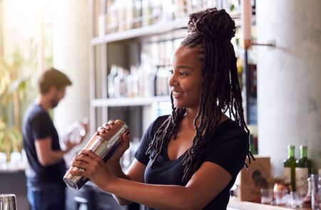 Female Bartender Mixing Cocktail In Shaker Behind Barの写真素材