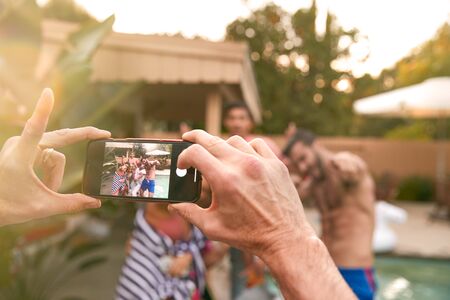 Group Of Friends Outdoors Relaxing By Swimming Pool Posing For Photo On Mobile Phoneの写真素材