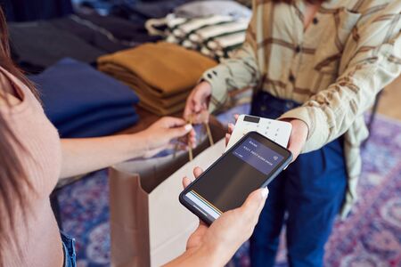 Woman In Clothing Store Making Contactless Payment With App On Mobile Phoneの写真素材