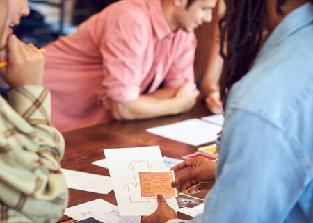 Close Up Of Fashion Designers Having Creative Meeting Around Wooden Table In Studio
