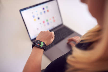 Close Up Of Woman Checking Health Activity App On Smart Watch At Home On Laptopの写真素材