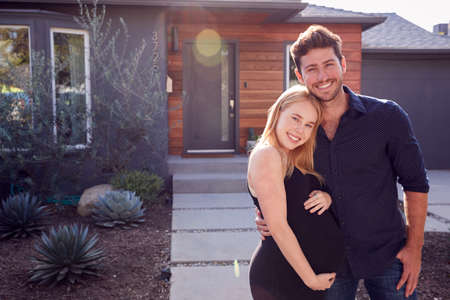 Portrait Of Couple With Pregnant Wife Standing Outdoors In Front Of New Homeの写真素材