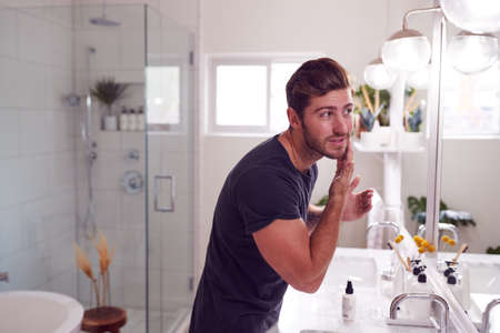 Man Wearing Pyjamas Standing At Sink Putting On Moisturizer In Bathroomの写真素材