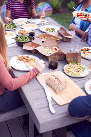 Close Up Of Friends In Garden At Home Sitting At Table Enjoying Food At Summer Garden Partyの写真素材