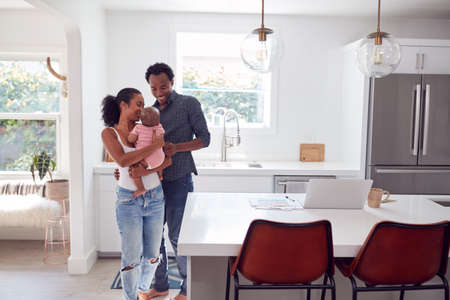 Family With Baby Daughter In Kitchen Using Laptop On Counterの写真素材