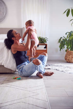 Loving Mother Playing With Baby Daughter Sitting On Floor In Bedroom