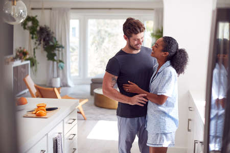 Loving Couple Wearing Pyjamas Hugging In Kitchen At Home Together